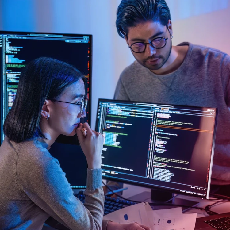 Due colleghi collaborano e guardano un pc con stringhe di codice di programmazione
