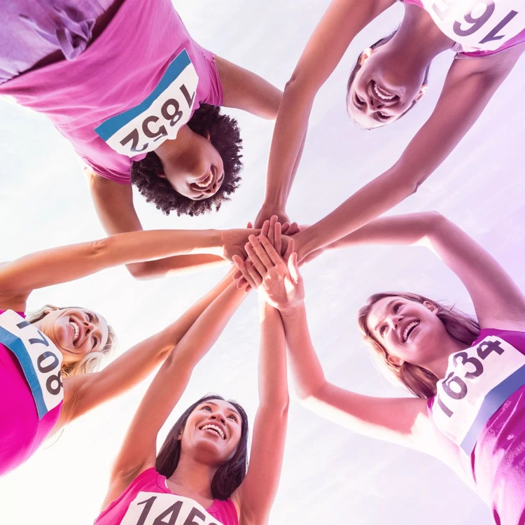 Un gruppo di ragazze con pettorine numerate unisce le mani e si fa forza a vicenda in senso di solidarietà e benessere.