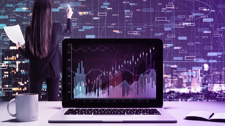 Una professionista di spalle analizza flussi di dati su una parete digitale mentre un laptop in primo piano mostra grafici statistici dettagliati, rappresentando l'integrazione di data & ai nei processi aziendali.