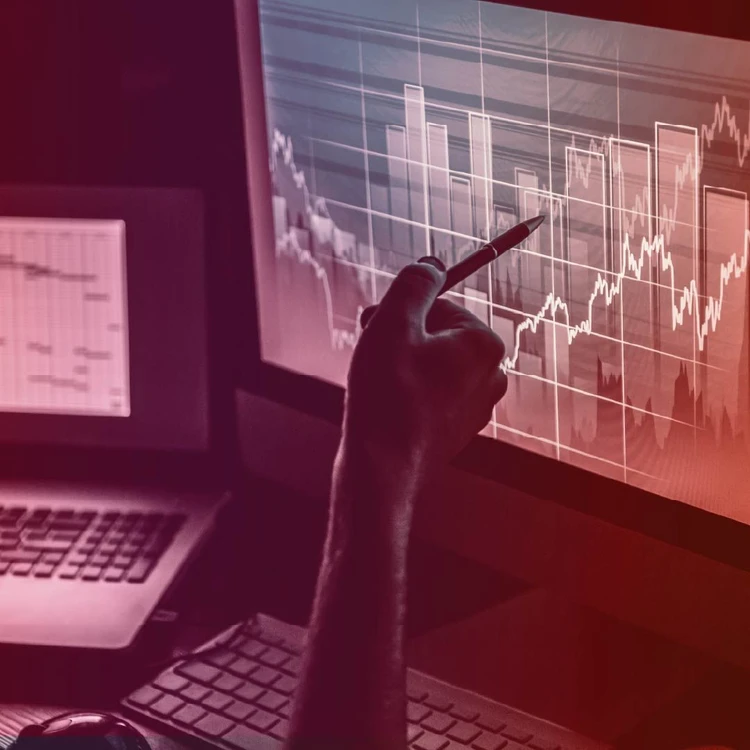 A hand holding a pen points to a bar and line graph on a computer screen.