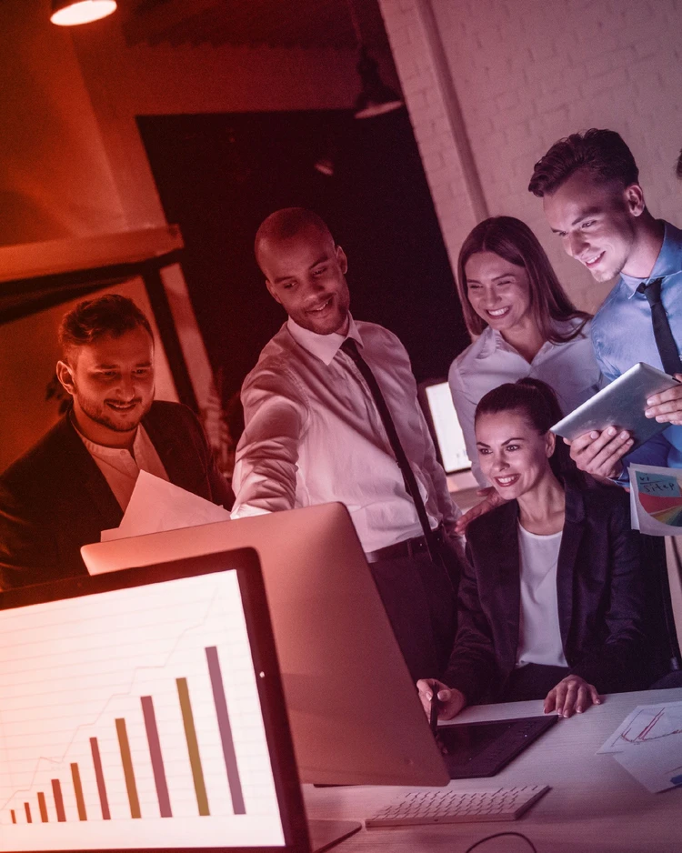 Un team di professionisti collabora davanti a un monitor che mostra grafici di crescita e analisi dati in un ufficio moderno.